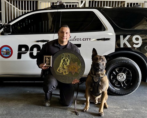 Officer Salazar holding trophies kneeling next to K9 Storm in front of a police vehicle